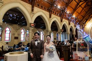 Wedding couple stands at the altar in a grand historic church with ornate arches and stained glass windows.