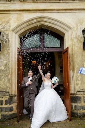 Newlyweds exit church doors under shower of confetti and bubbles.