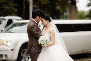 Elegant wedding couple poses together outside near white limousines with delicate blue bouquet.