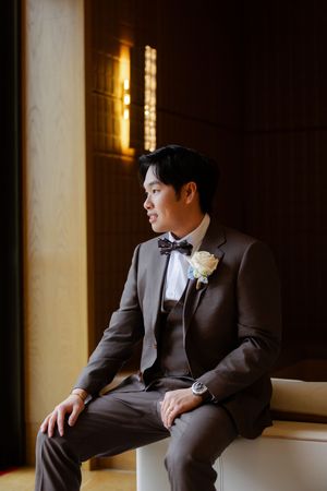 Classic formal attire with black bow tie and white boutonniere in window light.