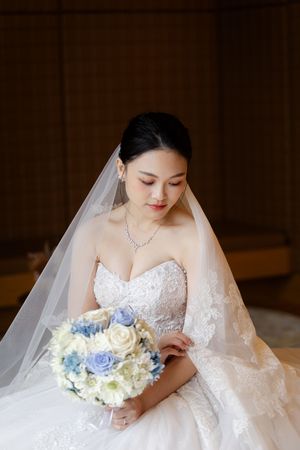 Close-up of bridal details showing white lace dress, veil, and blue and white bouquet.