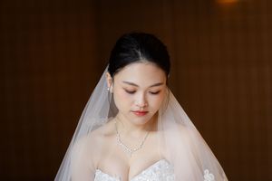 Close-up shot of bride in white gown and veil against dark background.