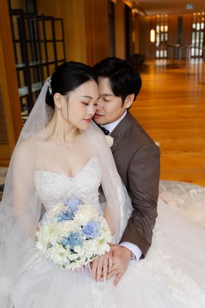 A couple in wedding attire share an intimate moment on a polished wooden floor in warm lighting.