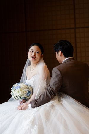 A bride in a flowing white gown holding a blue and white bouquet poses beside columns indoors.