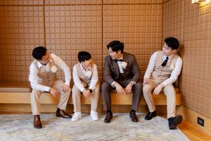 Row of wedding guests sitting against an orange tiled wall, showing only their legs and formal attire.