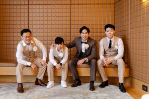 Groomsmen in casual attire sitting against orange tiled wall at wedding venue.
