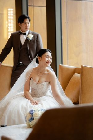 Bride in an elegant white strapless gown sits gracefully in a sunlit room with modern decor.