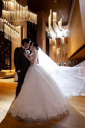 Wedding couple dancing in a grand ballroom with hanging crystal chandeliers and warm ambient lighting.