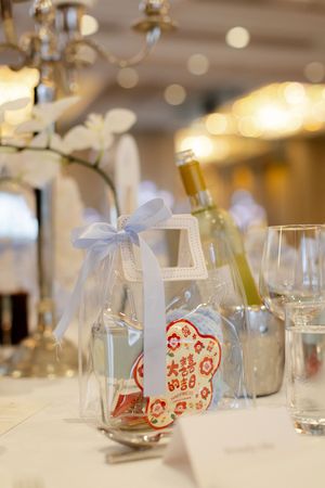 A decorative wedding favor with red Chinese symbols tied with white ribbon sits on an elegant table setting.
