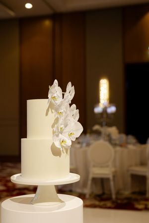 An elegant white wedding cake decorated with delicate white orchids displayed on a pedestal.