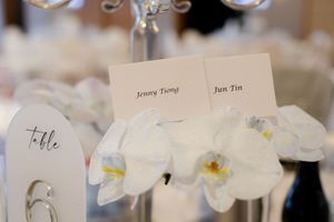 Wedding place cards with elegant calligraphy names sit among white orchid flowers on a table setting.