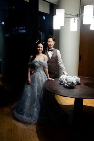 A couple in evening wear poses beside a round table with blue floral centerpiece.