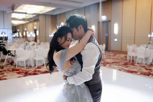 A couple dances together in an elegant ballroom setting with white tables and chairs in the background.