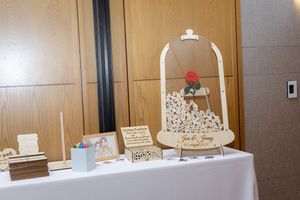 A white wedding guest book display with decorative arch and rose accent on a covered table.