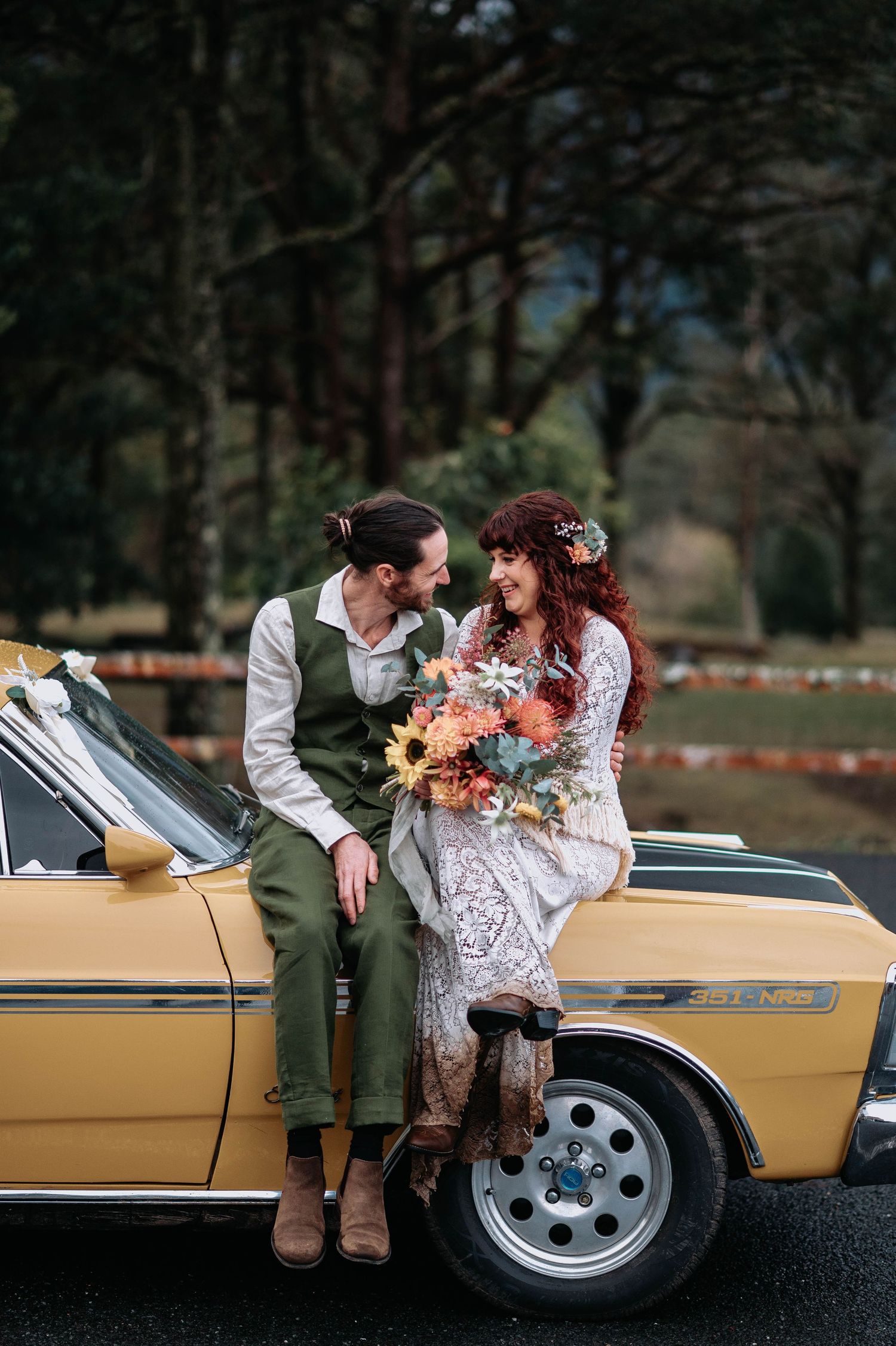 A couple in vintage-inspired wedding attire share an intimate moment outdoors, with the bride wearing a lace dress.