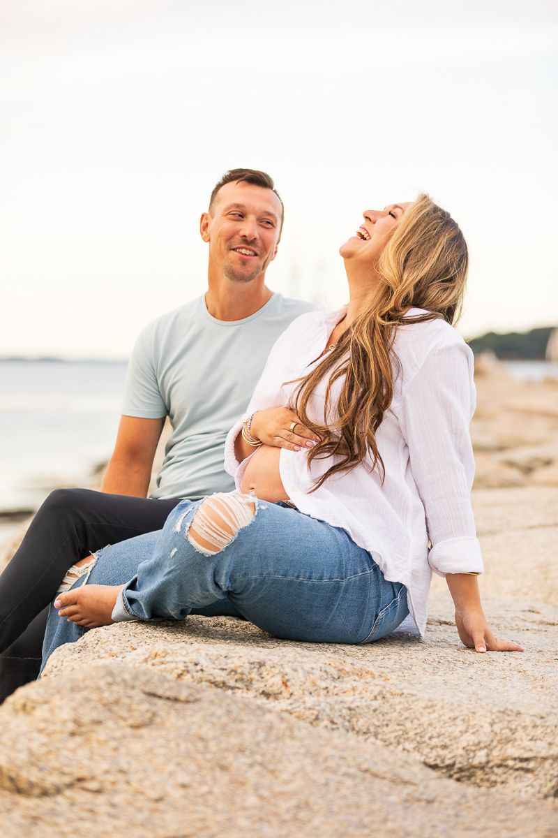 Couple laughing and enjoying time together on rocky beach during sunset.