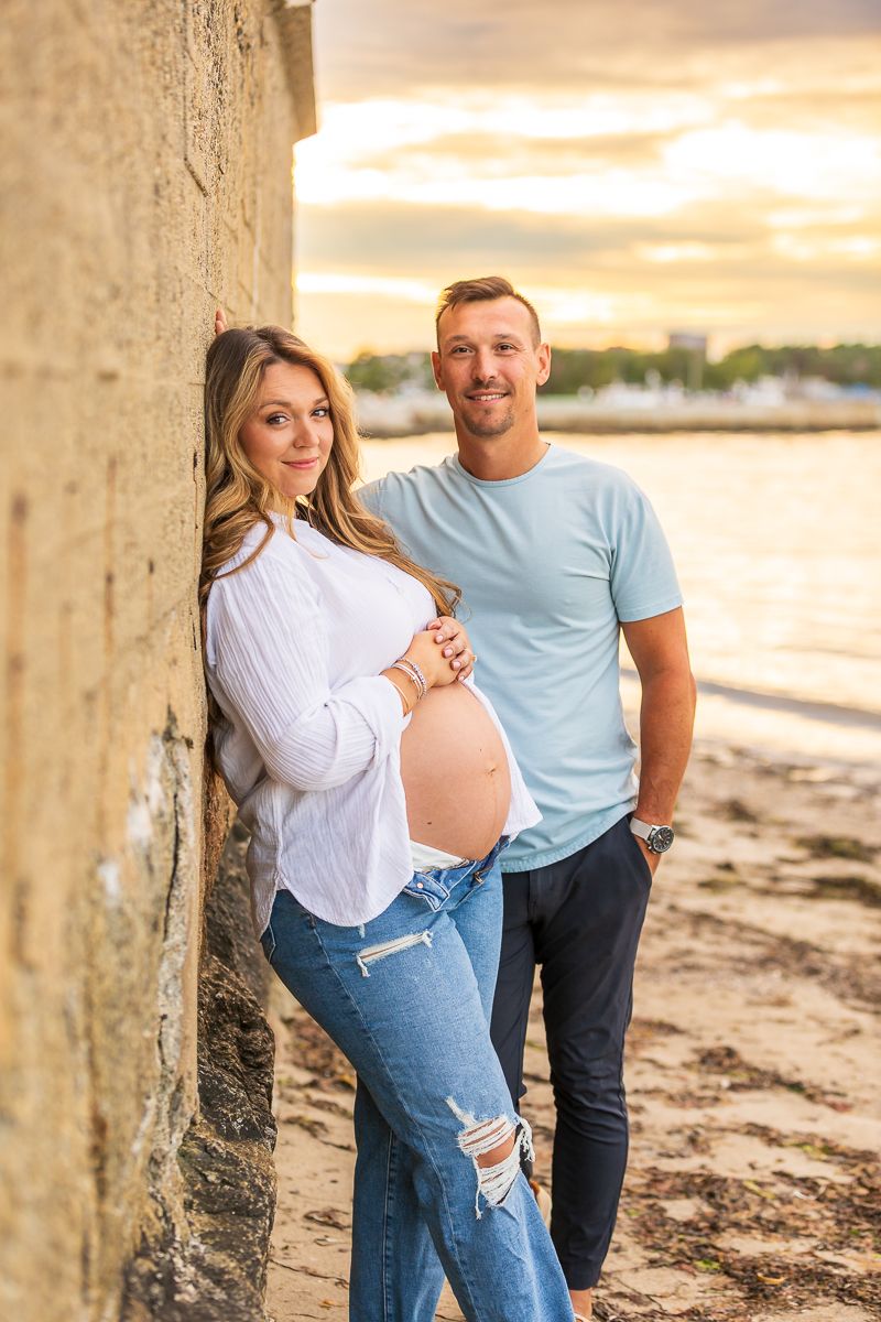 Expectant couple pose for maternity photos on beach at golden hour.