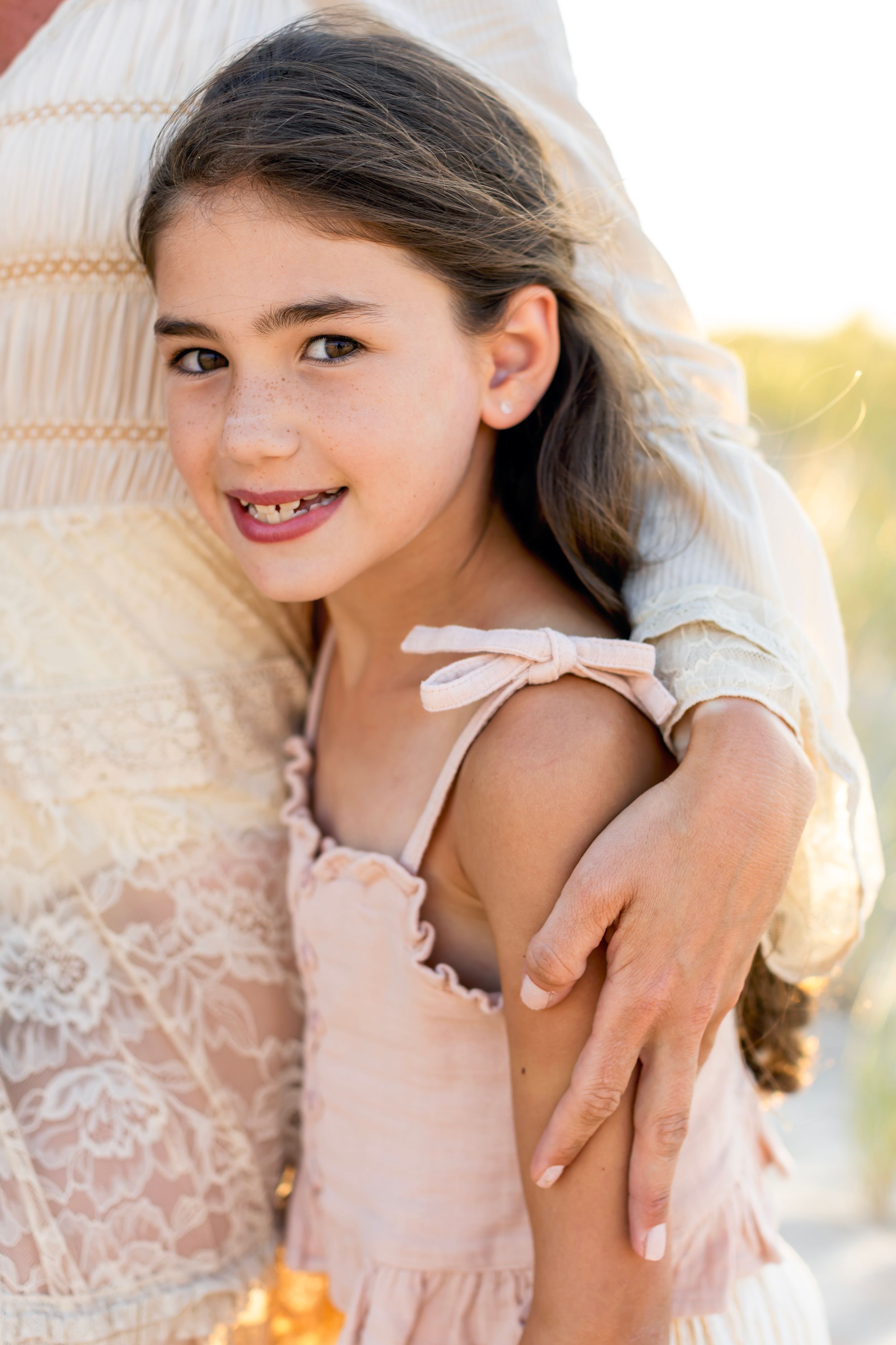 Young figure in delicate lace dress poses candidly in dreamy golden sunlight.