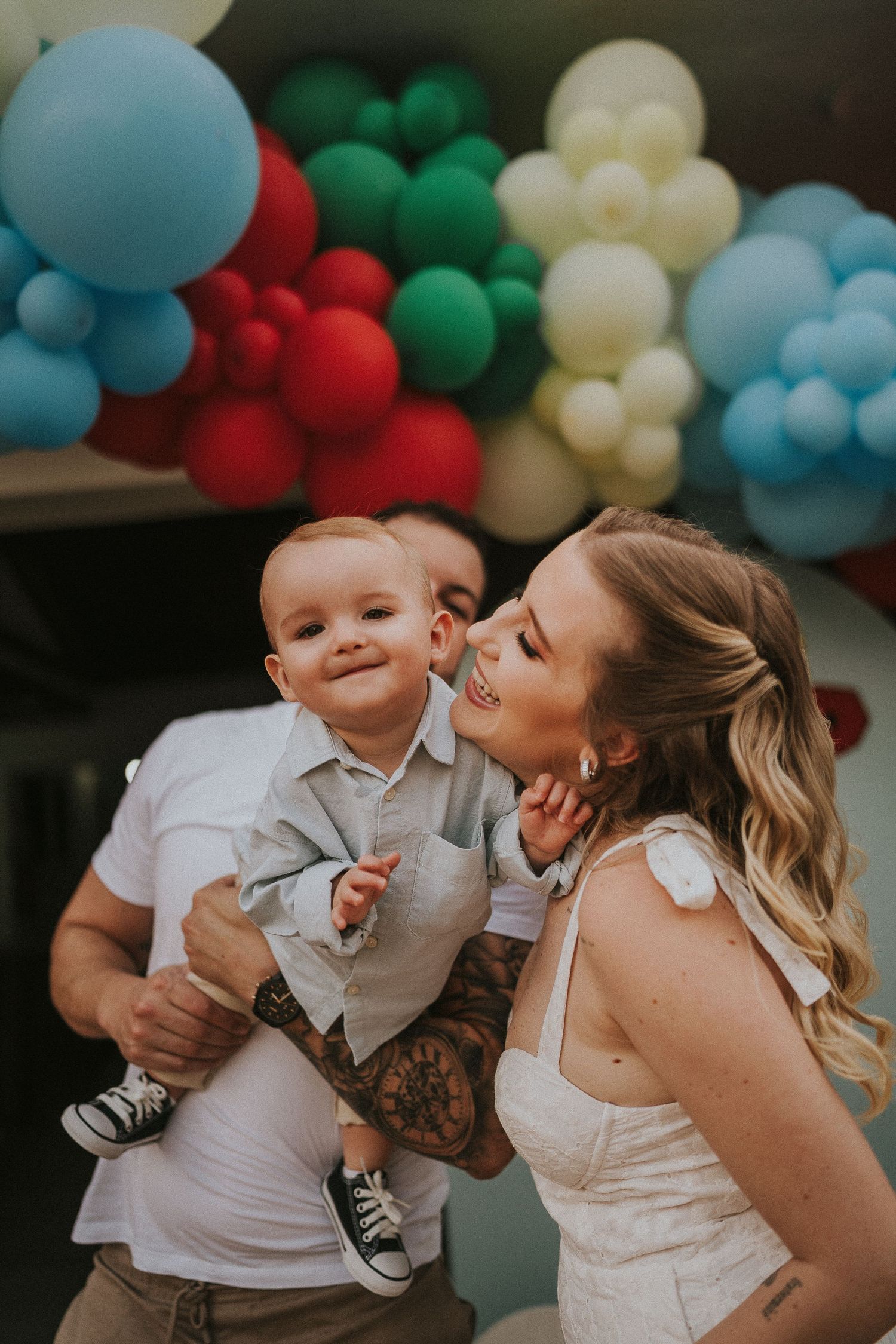 Festive outdoor party scene with colorful balloon arch and tender moment between two people.