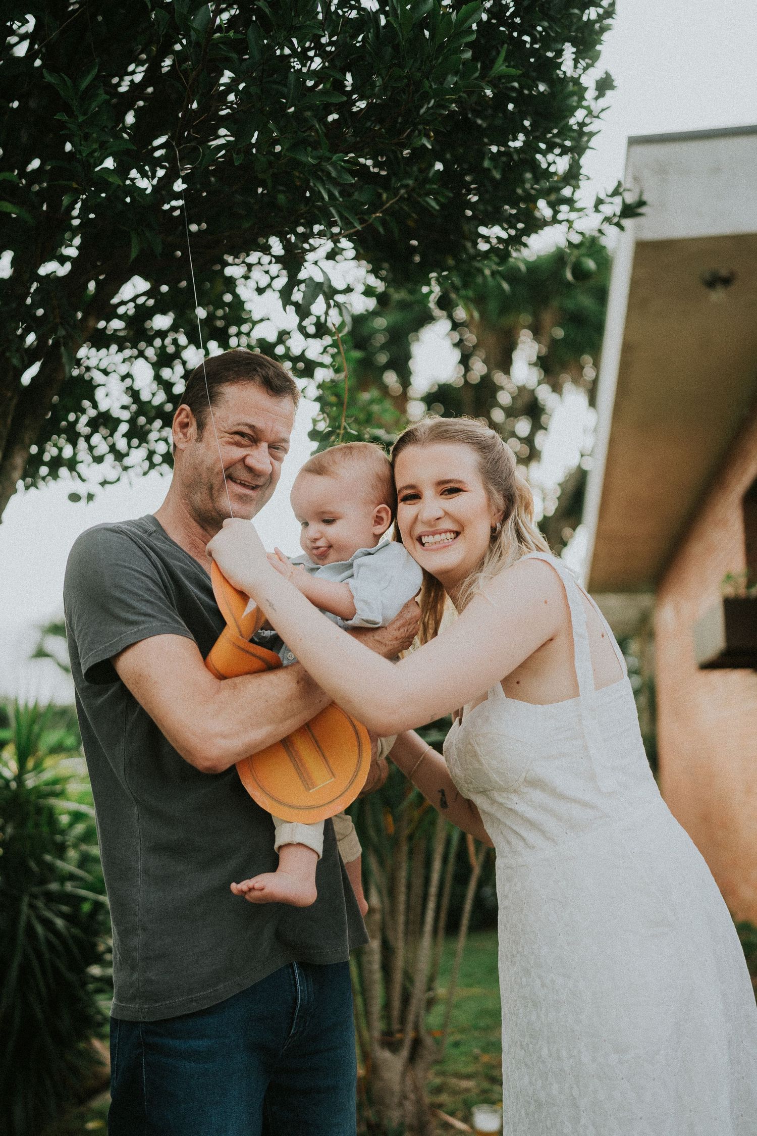 A couple outdoors shares a joyful moment with their baby under a tree.