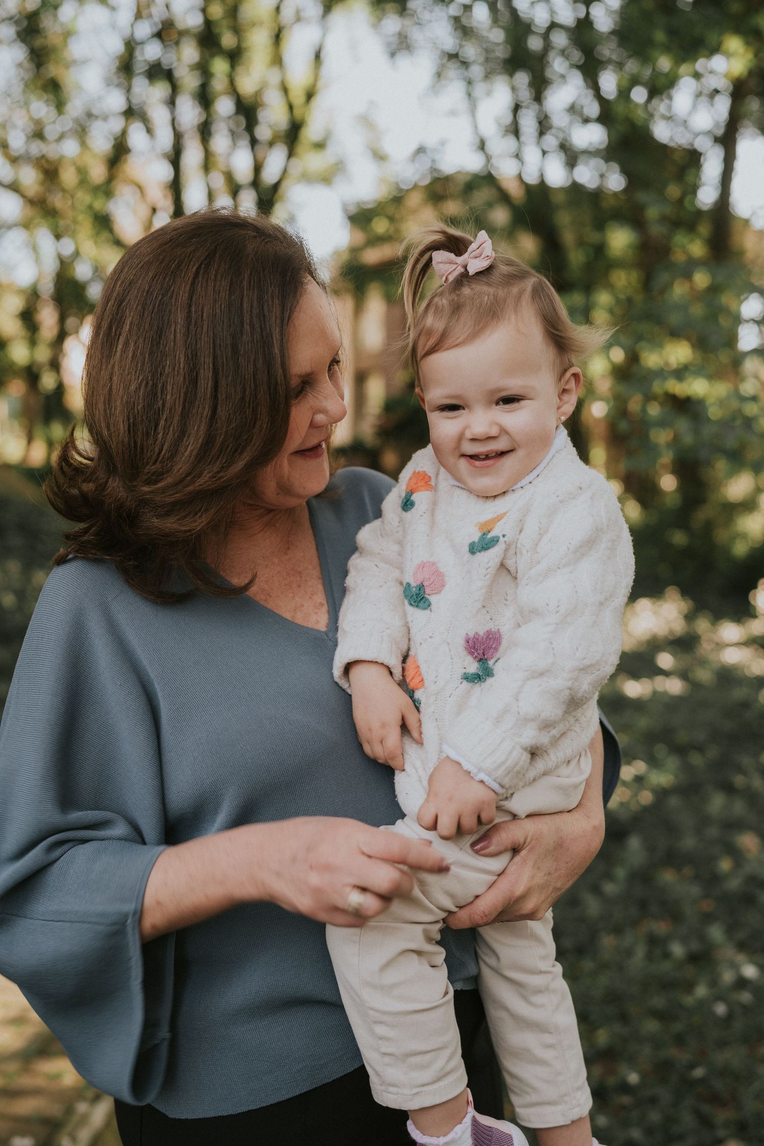 Tender outdoor portrait of a caregiver sharing a loving moment with a smiling toddler.