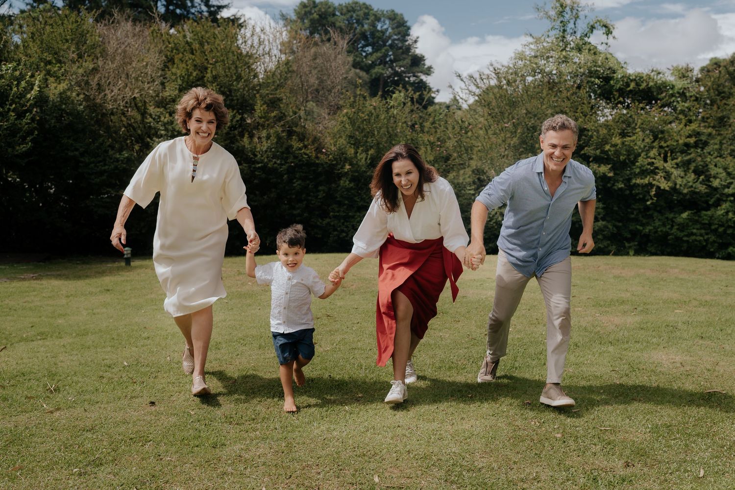 Family of four running and playing together on green grass outdoors.