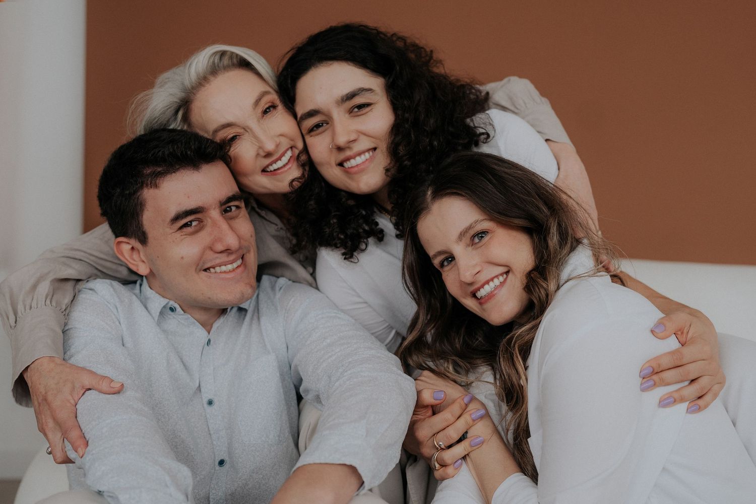 Portrait session with group wearing white and gray tones smiling and embracing together.