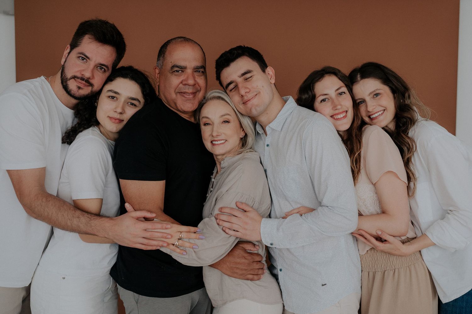 Group photo session with family members dressed in neutral colors hugging and smiling.