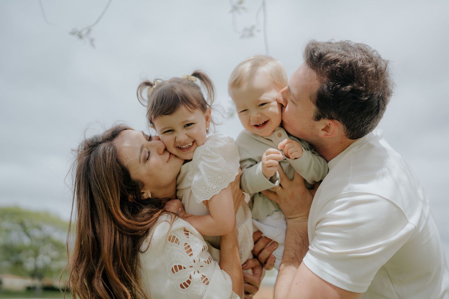 A joyful family moment captured in soft lighting as parents share loving embraces with their young children.