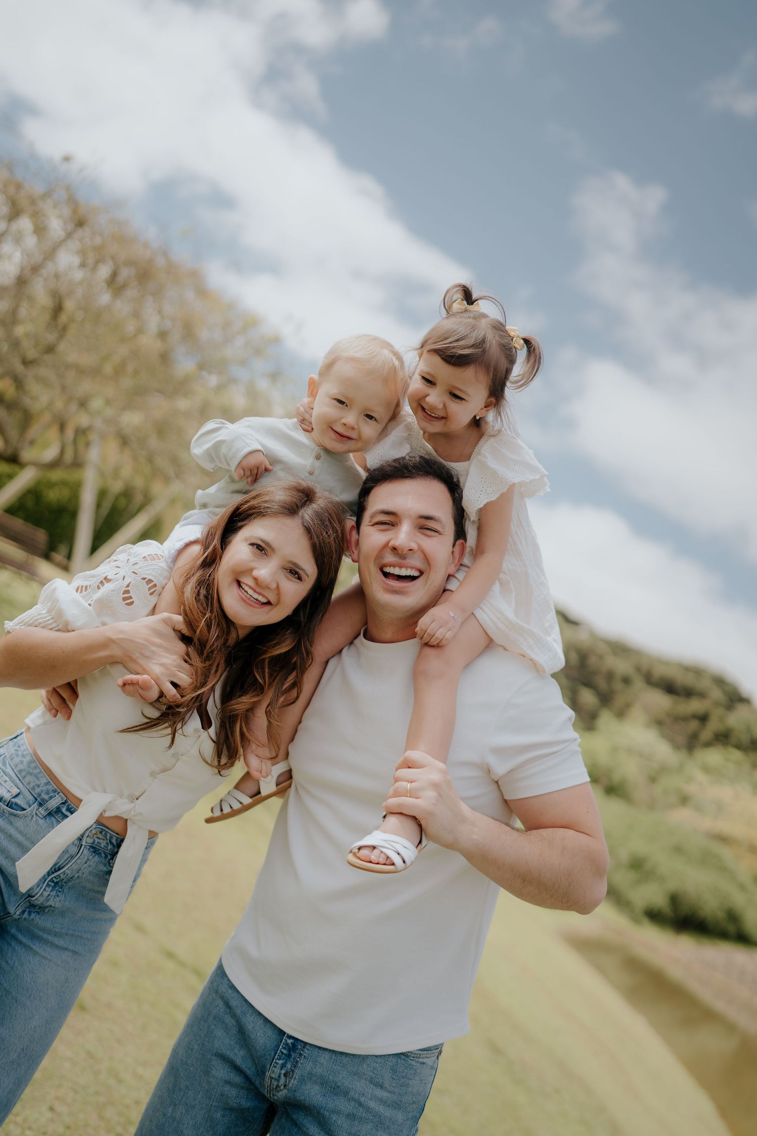 Playful outdoor family photoshoot on grassy hill under blue sky.
