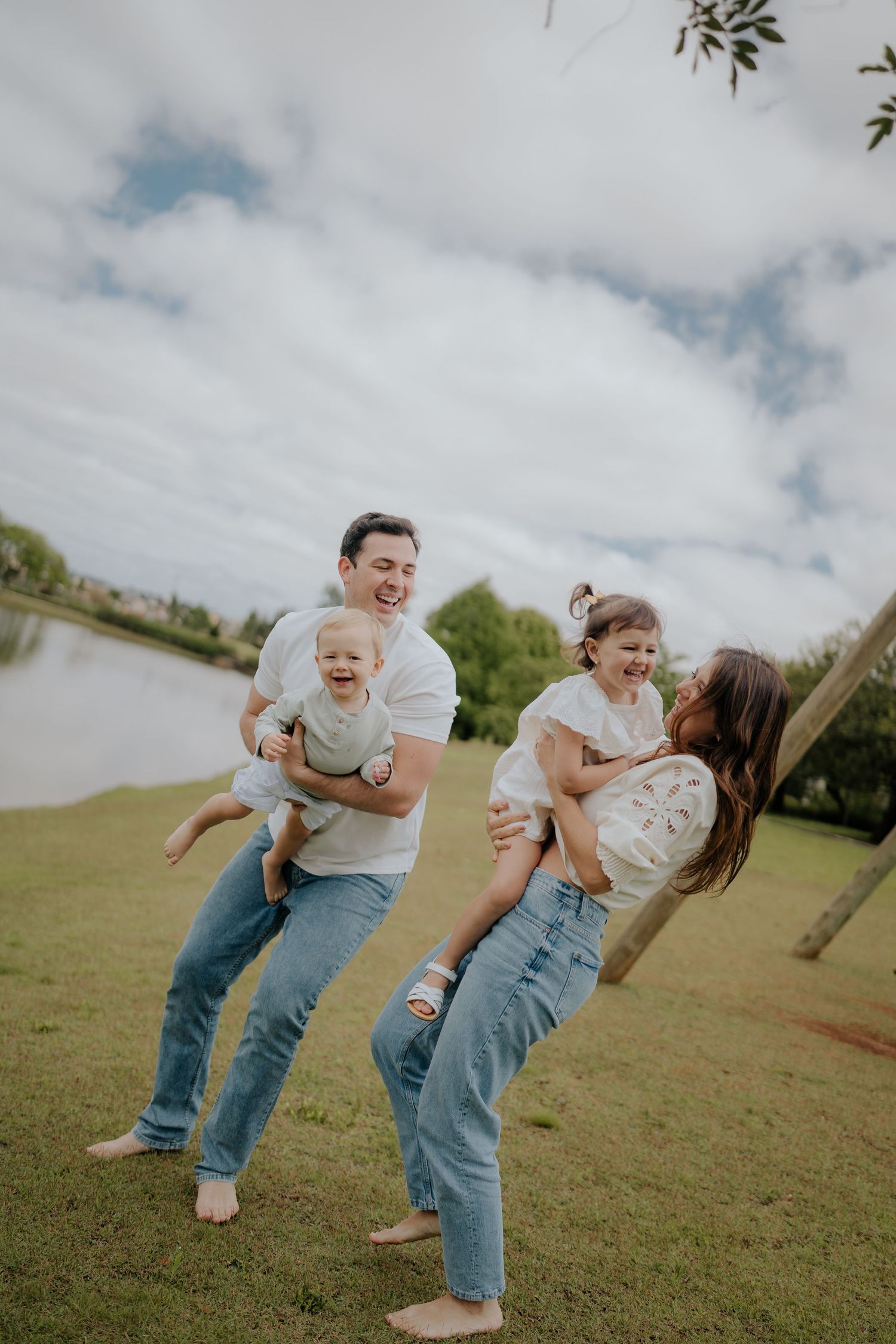 Candid family moments captured in grassy field with cloudy sky backdrop.