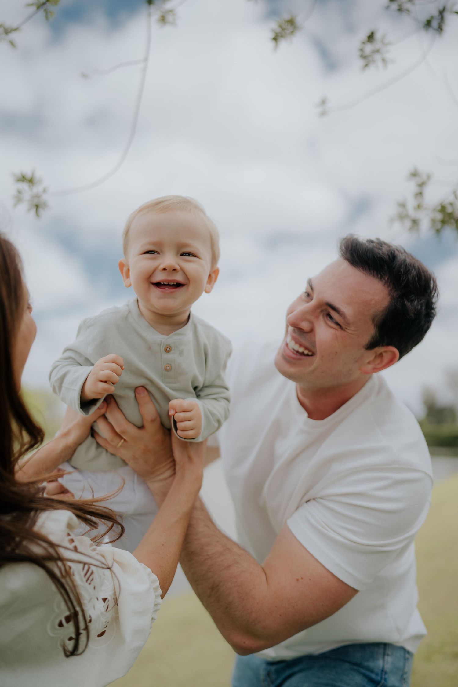Candid expressions during outdoor family photoshoot with cloudy sky background.