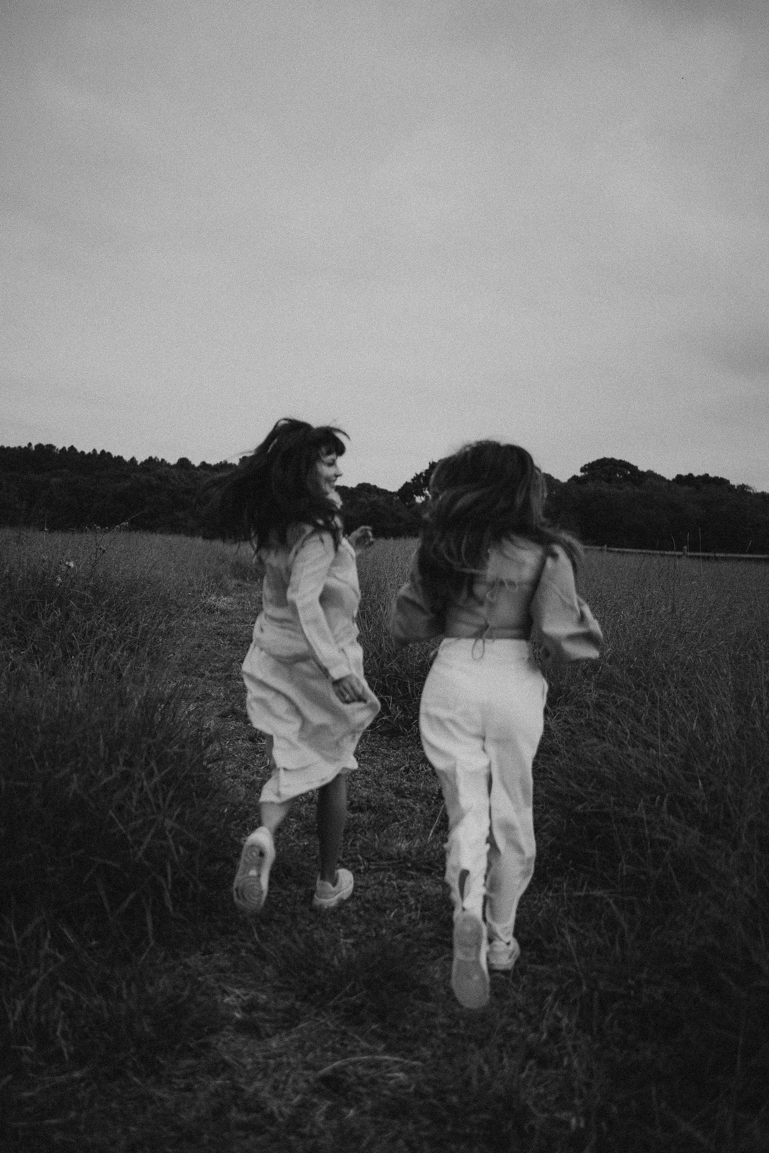 Two people in white clothing running playfully through a field in black and white.