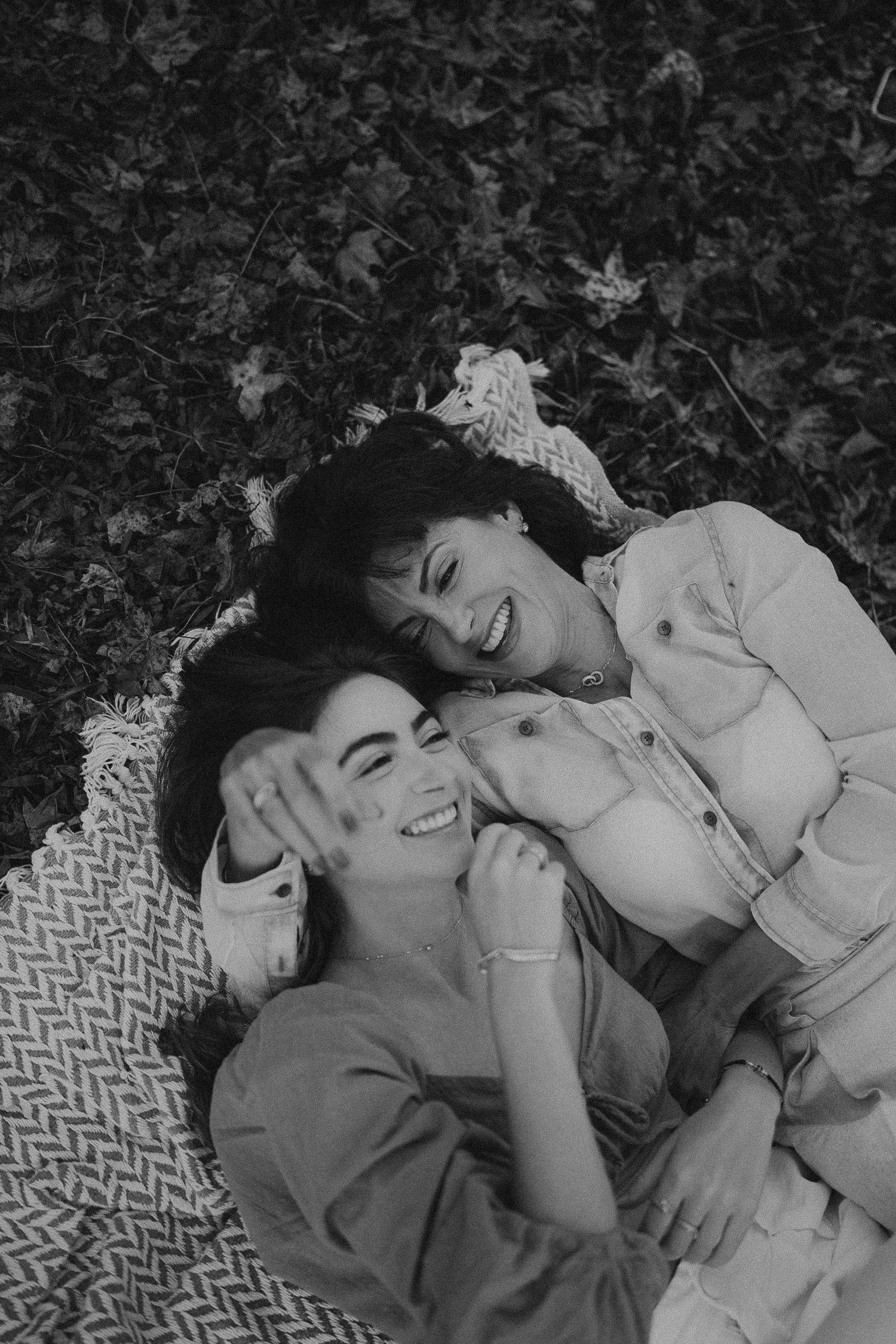 A black and white photo of two friends lying on a blanket outdoors sharing genuine laughter.