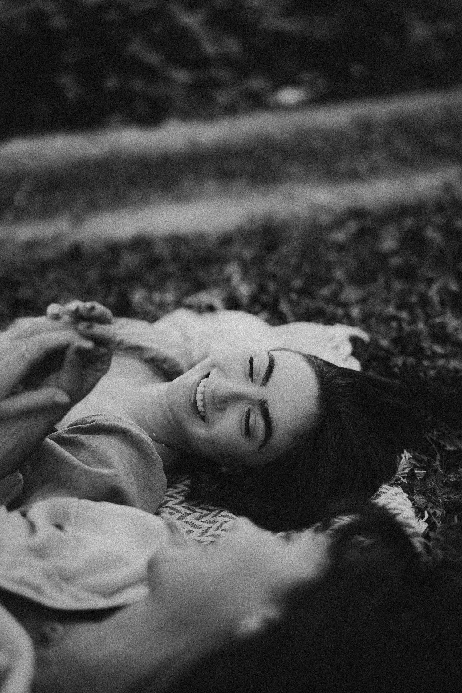 A candid black and white photo of two friends lying on grass and enjoying a moment together.