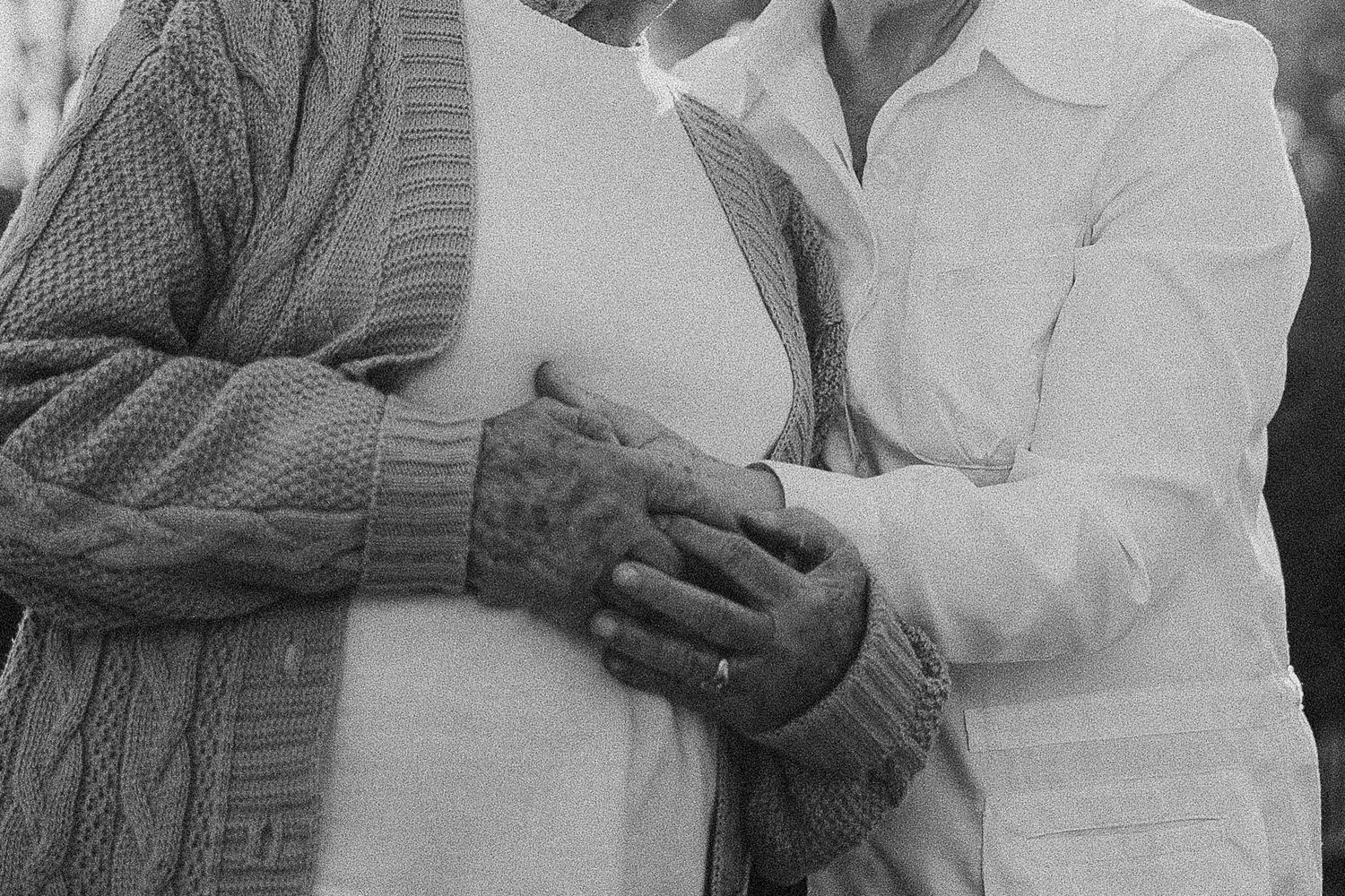 Two people in contrasting sweater and shirt embracing outdoors in black and white.