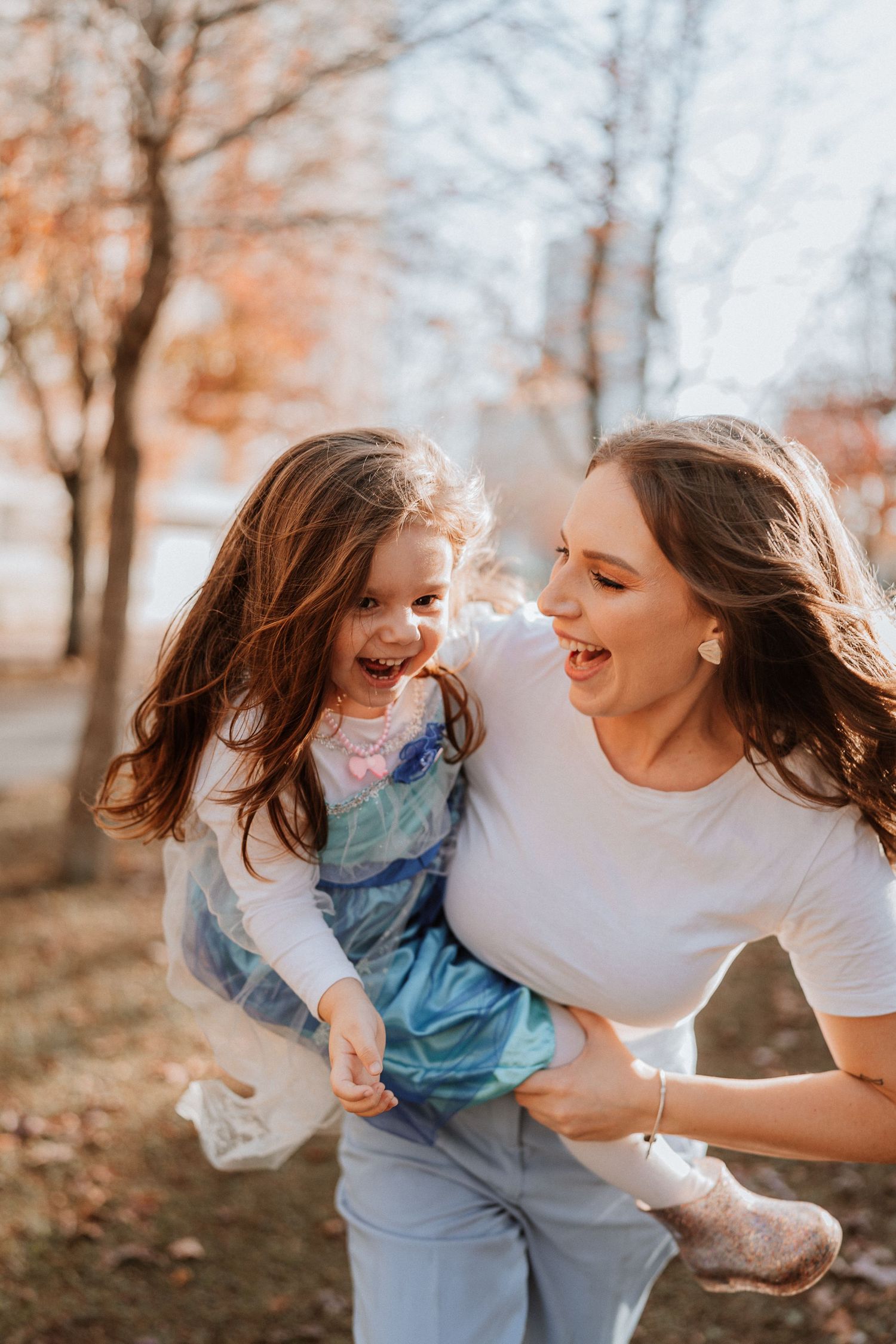 Mother and daughter sharing playful moment in autumn setting with natural lighting.