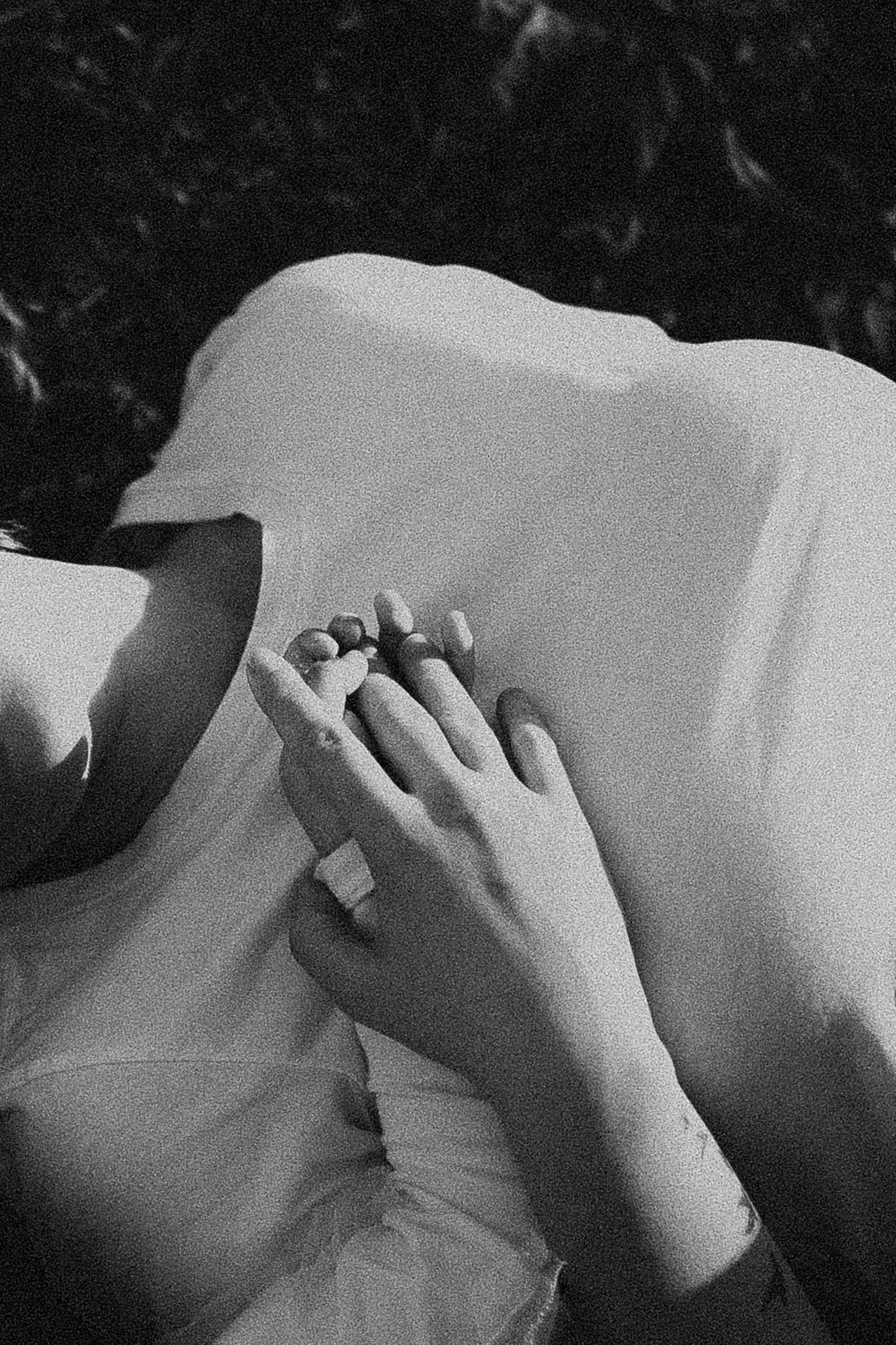 Close-up of hands clasped together on white fabric with an engagement ring.