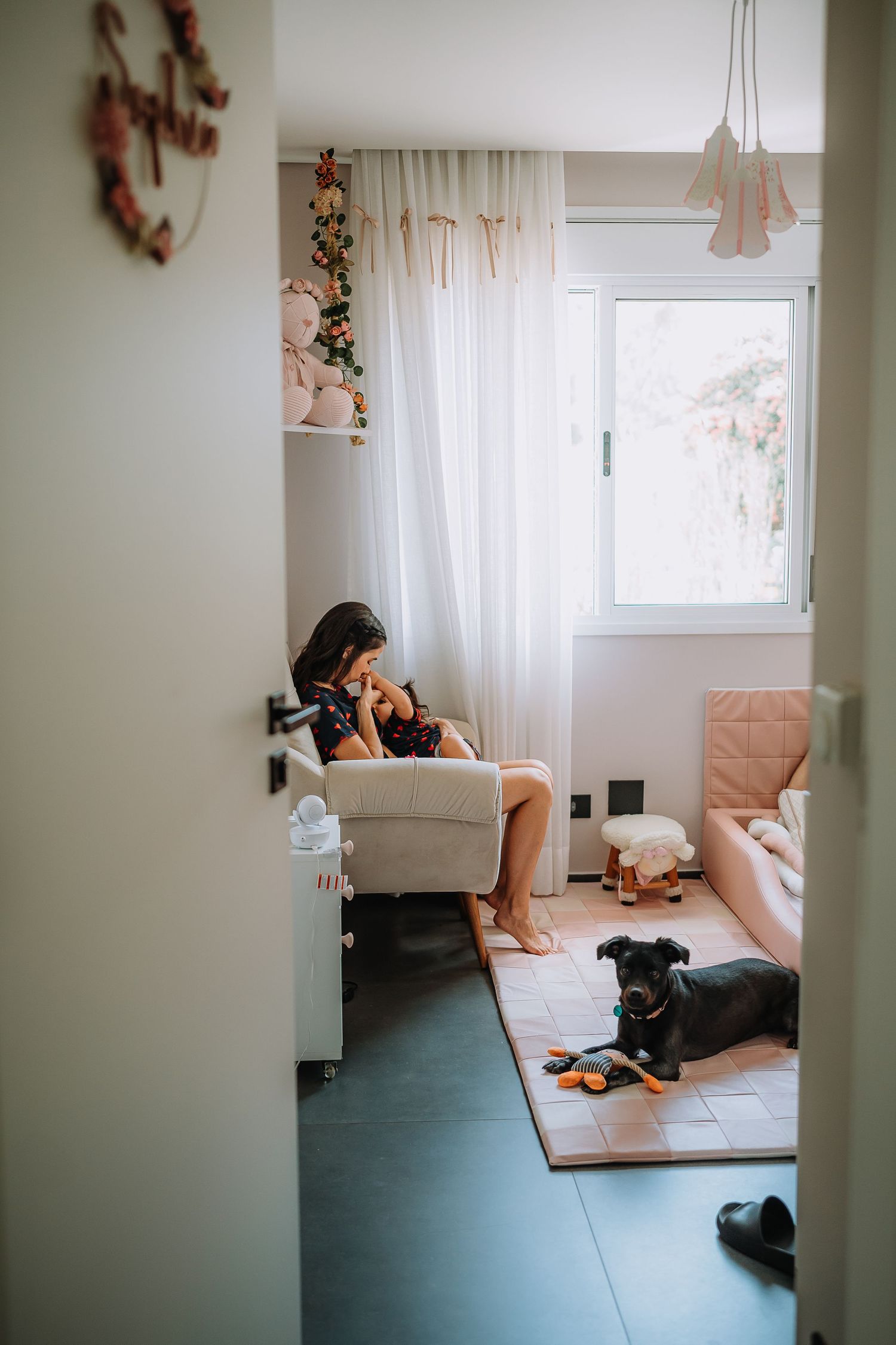 A cozy nursery room scene with a person sitting in a chair while a dog rests on the floor.