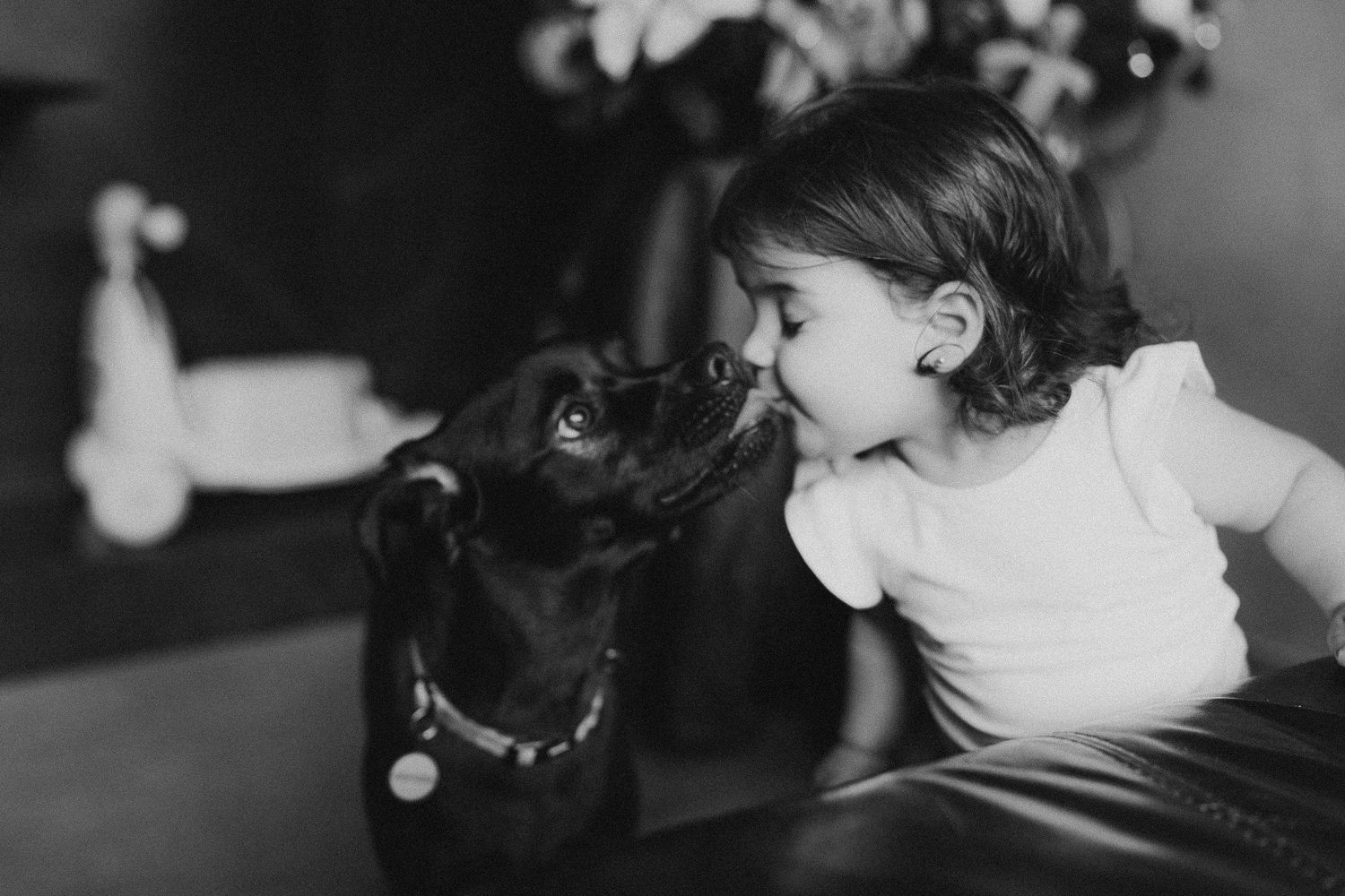 A small child and black dog share a sweet nose-to-nose moment in black and white.