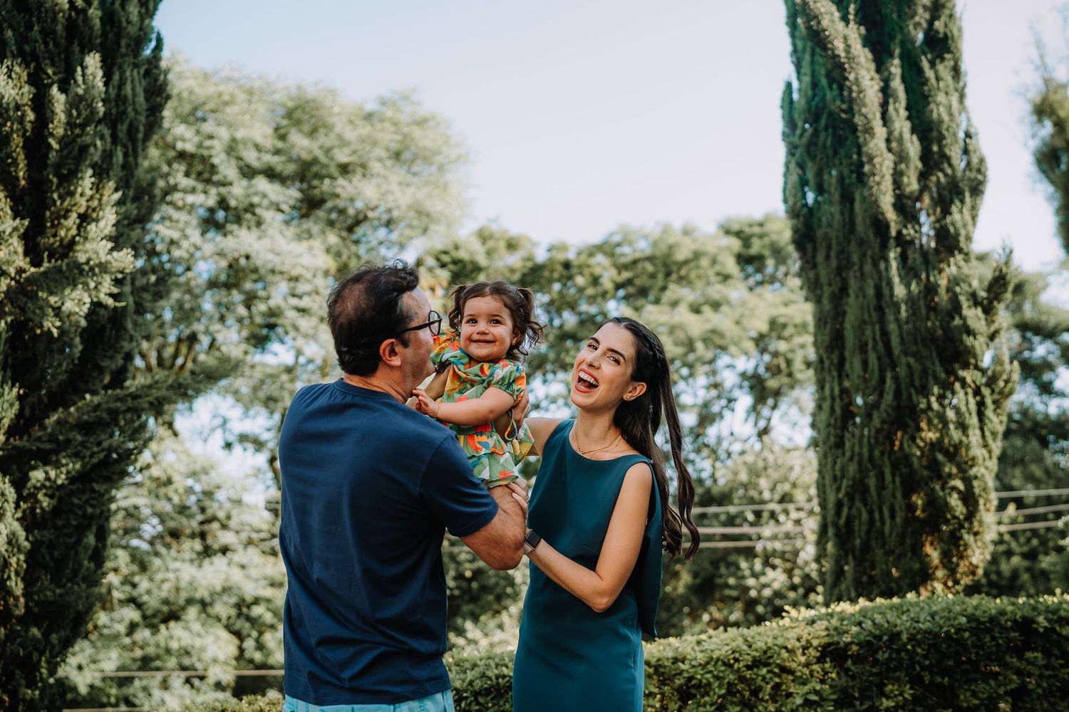A family shares a playful moment together outdoors among cypress trees.