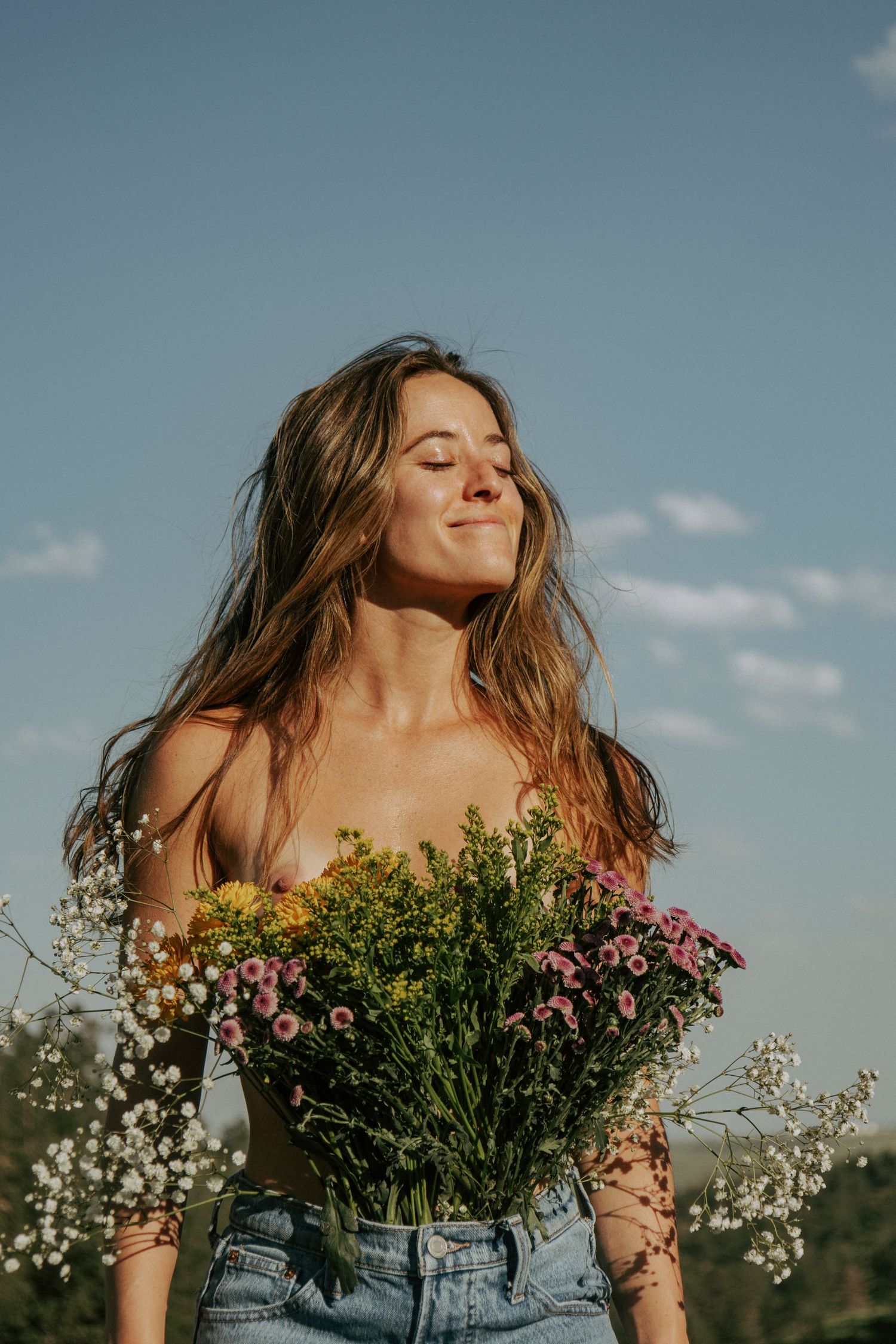 A person in denim holds a vibrant bouquet of wildflowers while enjoying a sunny day outdoors with blue skies.