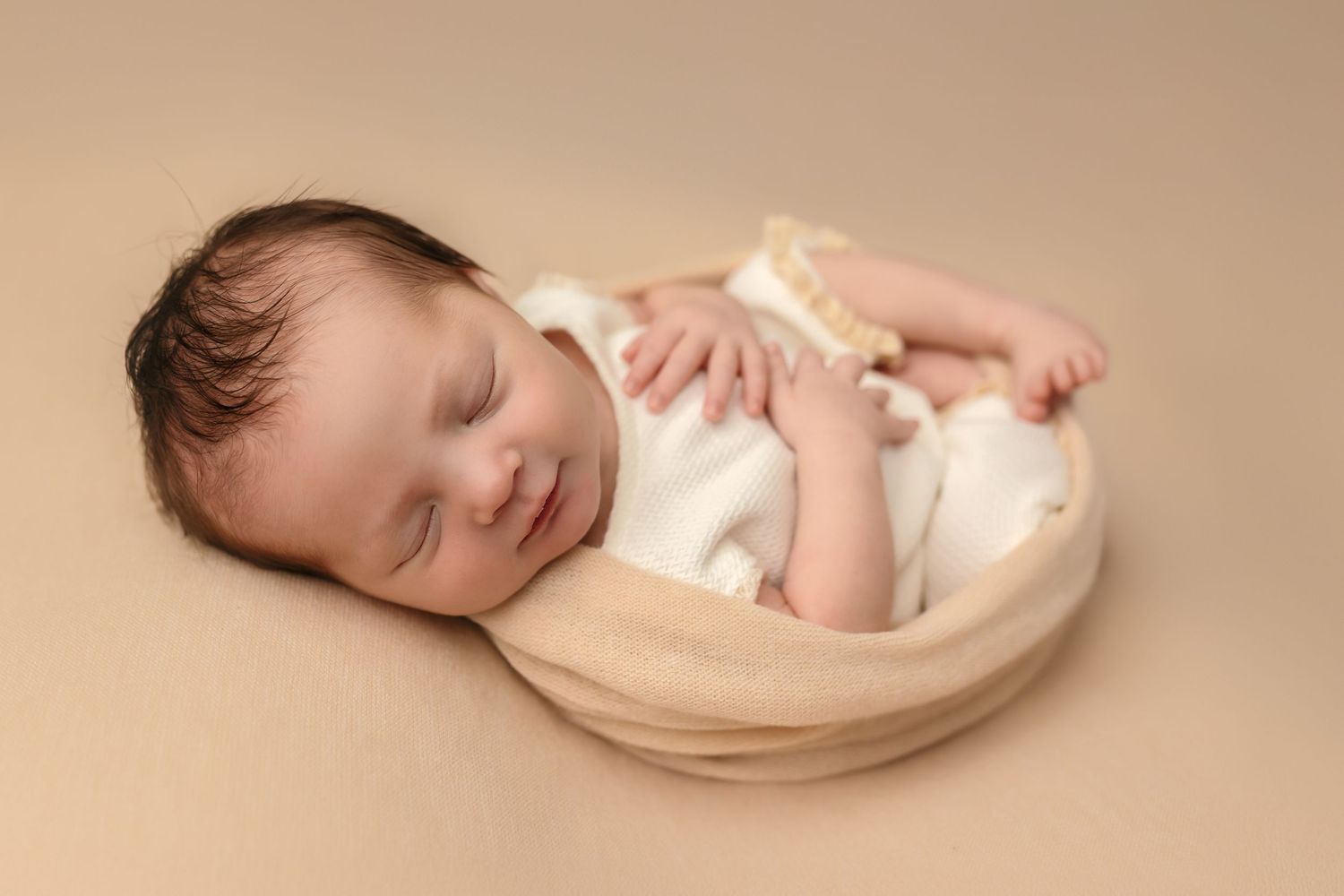 Newborn girl wrapped in a warm vanilla blanket smiles softly during a sweet moment captured by a Charlottesville newborn photographer.