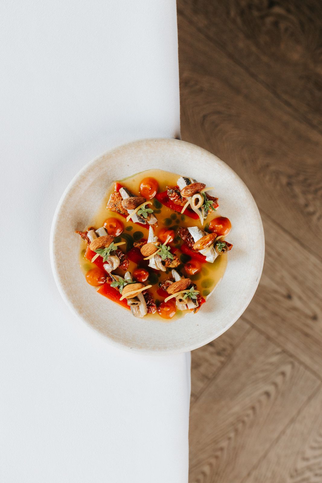 Elegant restaurant dish with cherry tomatoes, seafood, and fresh herbs in golden broth on a ceramic plate.