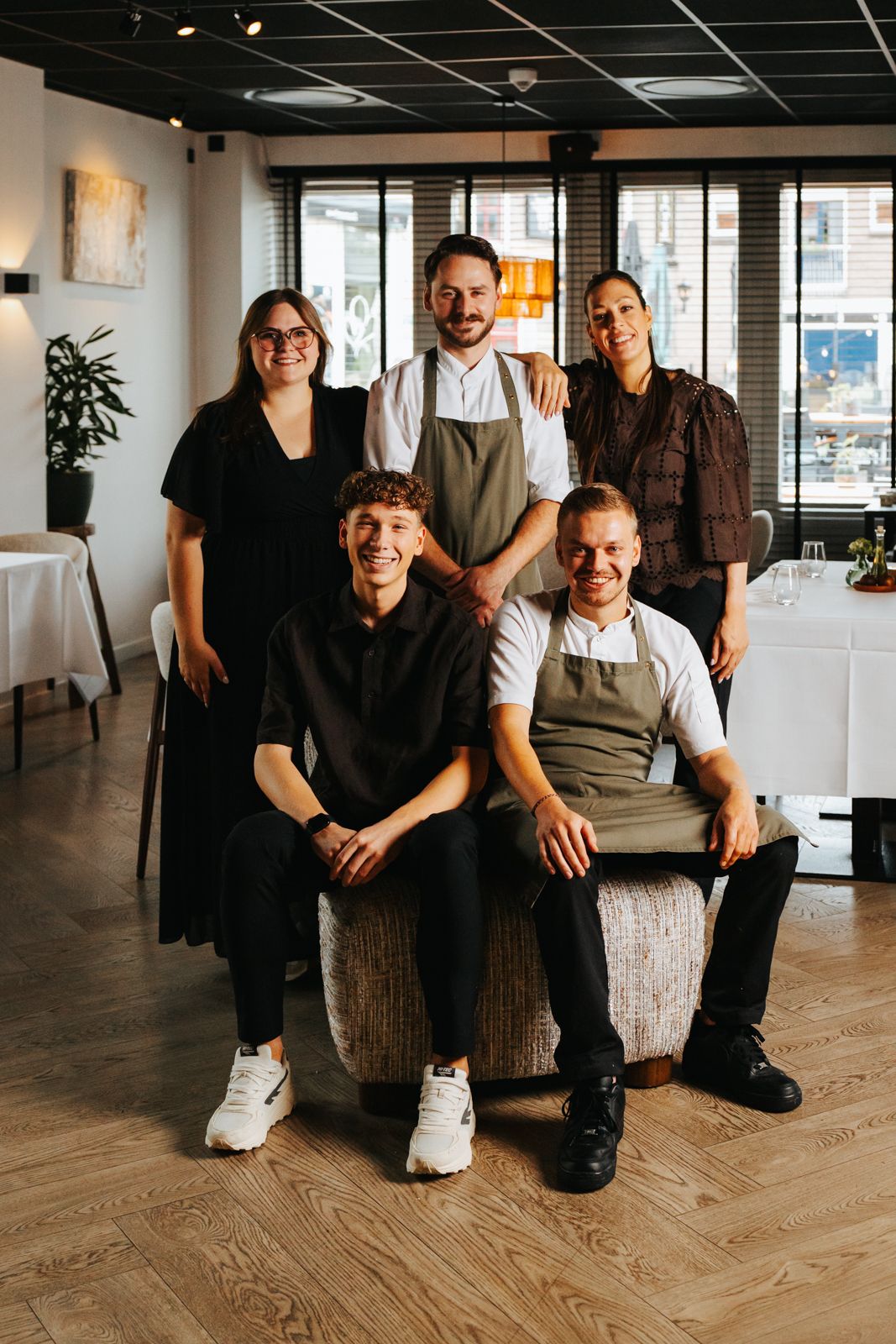 Five restaurant staff members pose together in an elegant dining room with white tablecloths and wooden floors.