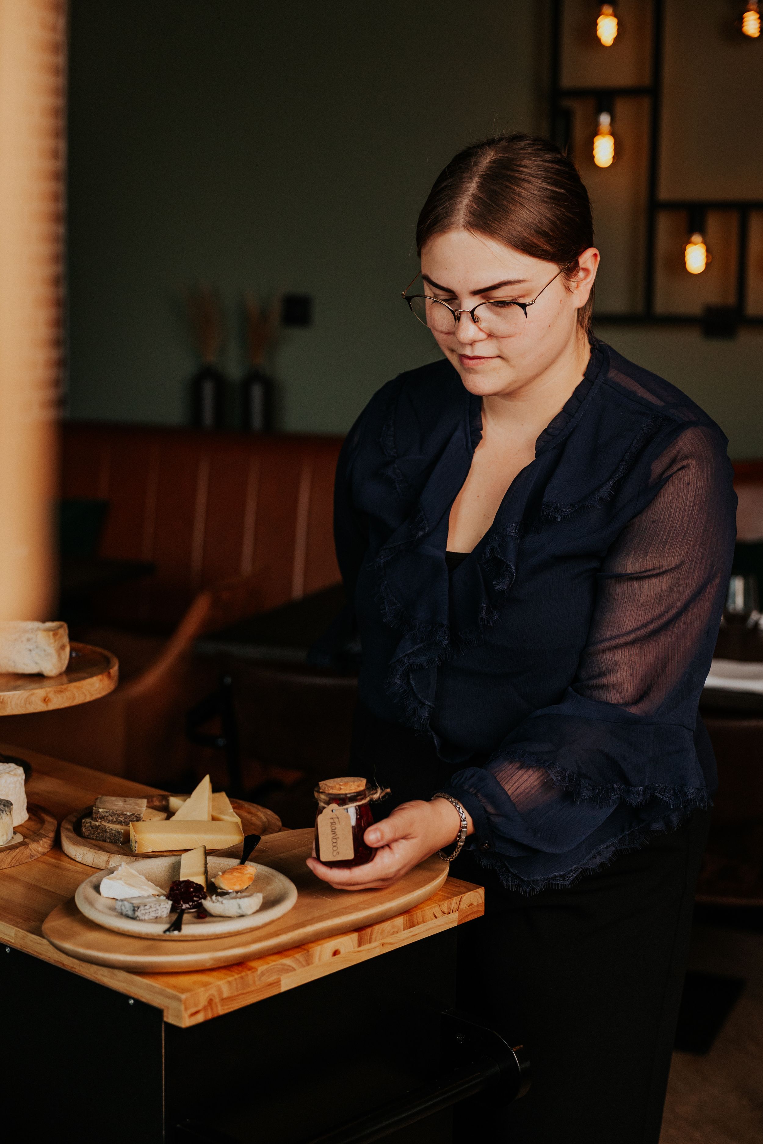 Server preparing food service on wooden serving board in dimly lit restaurant.