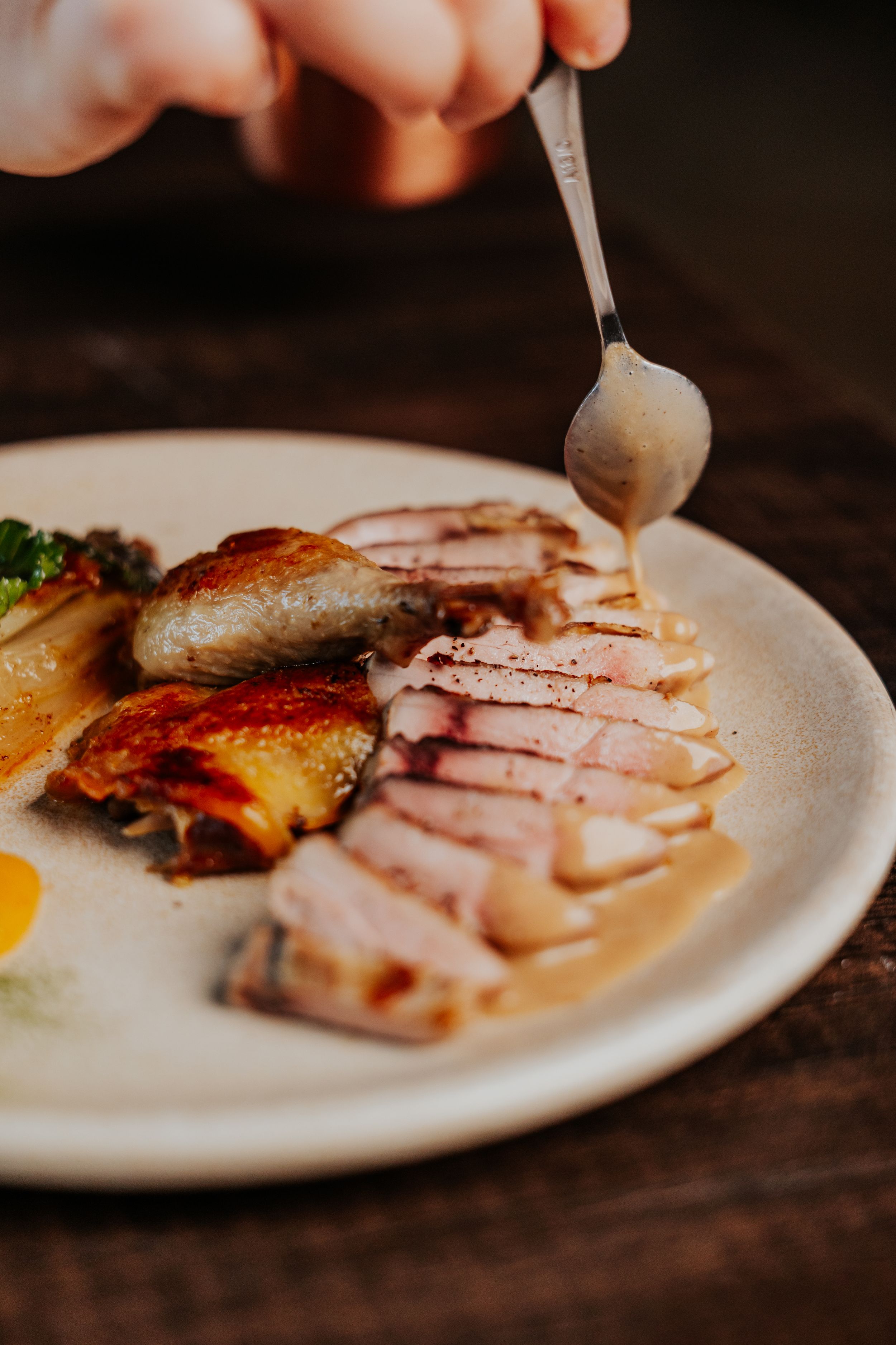 Sliced meat dish served on a white plate with garnish and sauce being drizzled from a spoon.