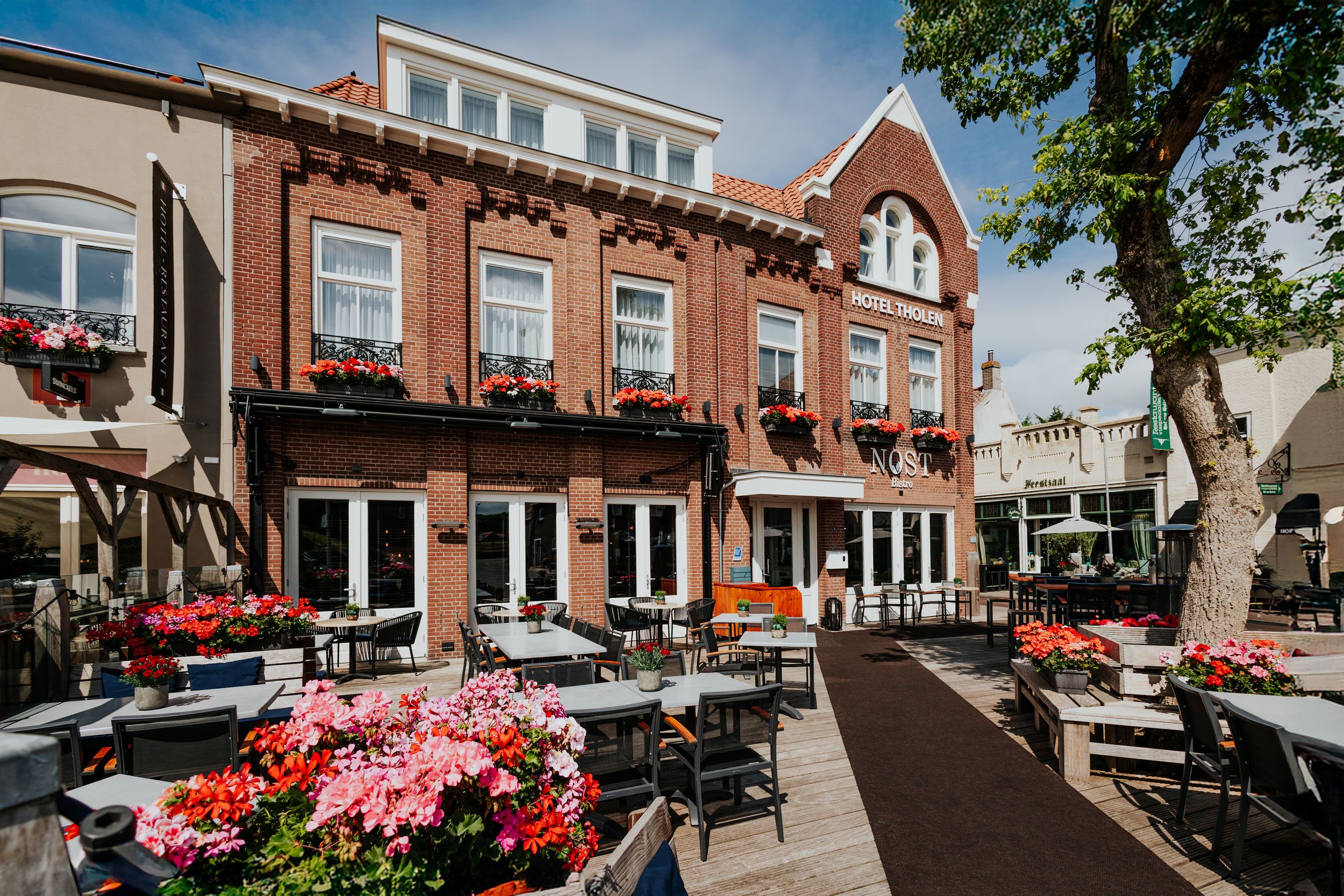 Exterior view of traditional Dutch buildings with red flowers and outdoor seating areas.