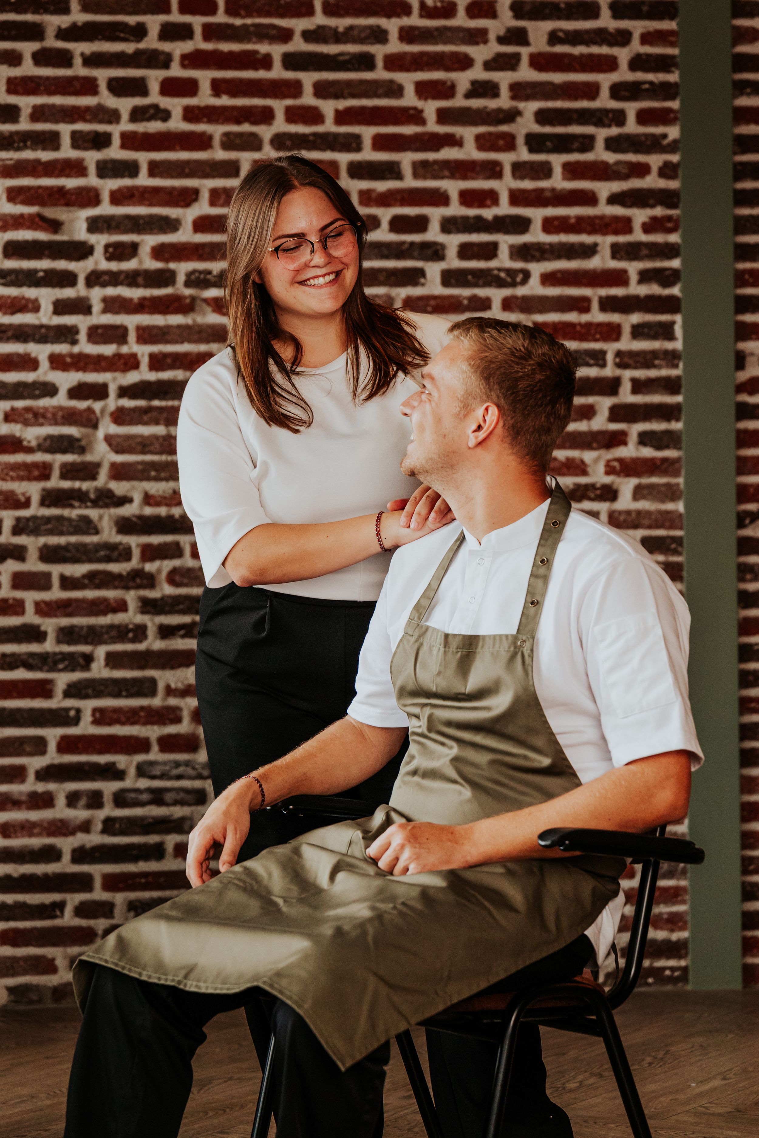 Two people sharing a casual moment against a rustic brick wall background.