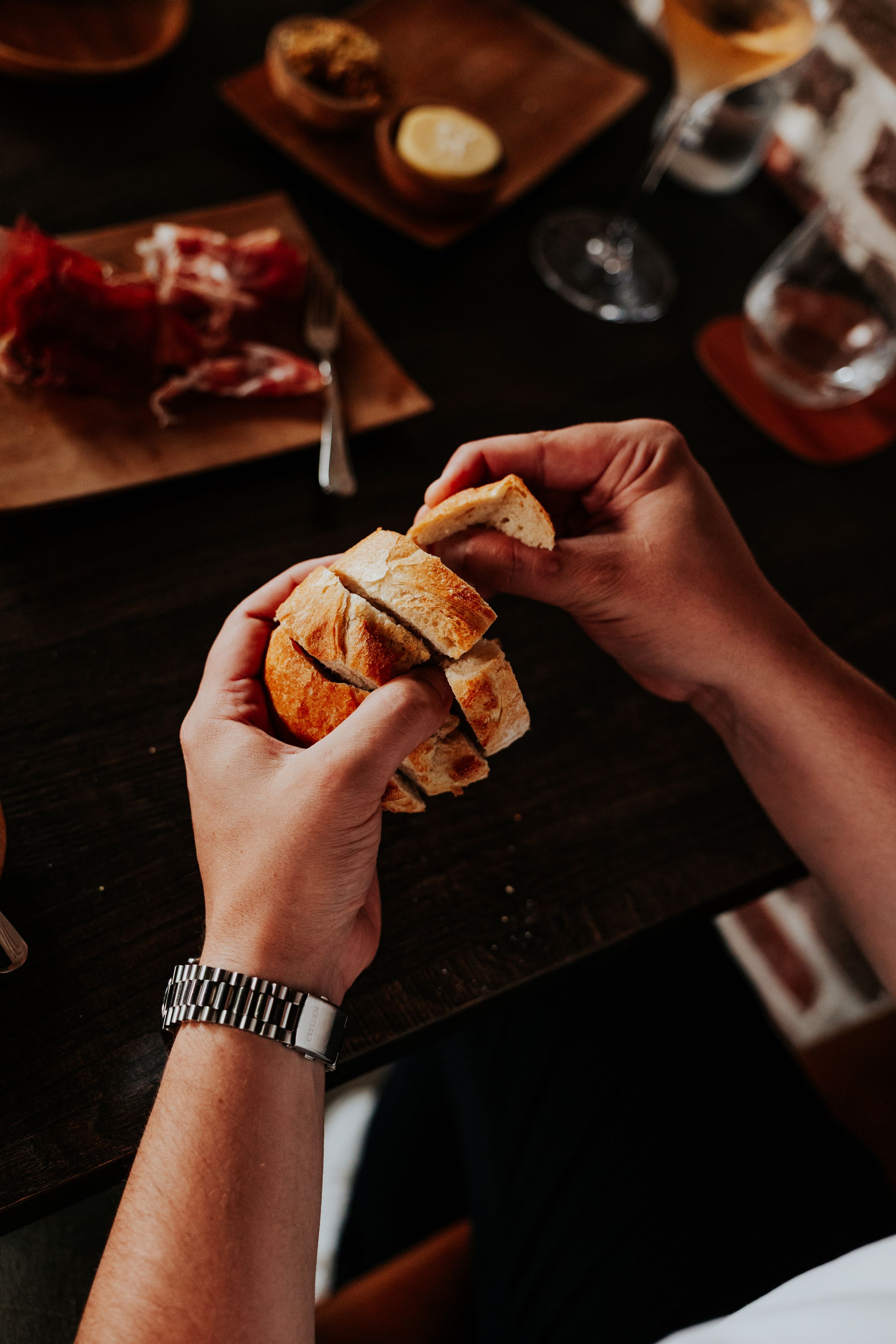 Hands holding and eating sandwiches in a dark moody setting with drinks in background.